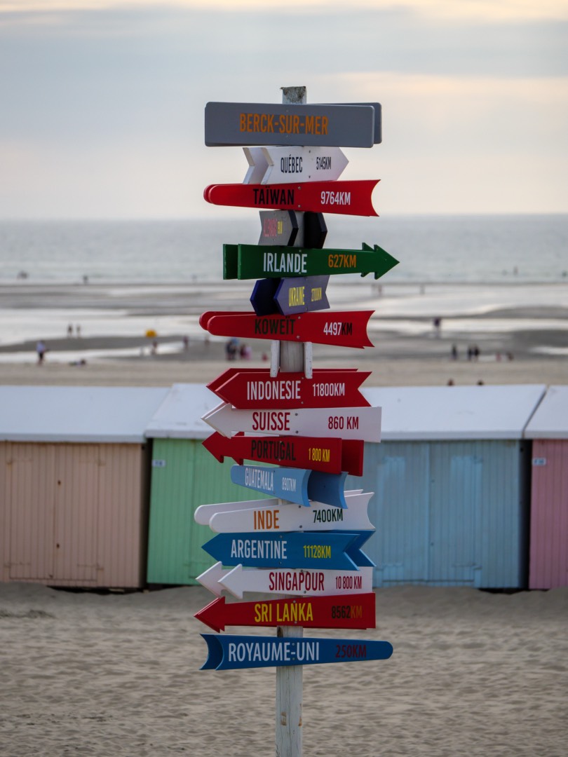 Panneau au bord d’une plage indiquant de nombreuses destinations touristiques à travers le monde.